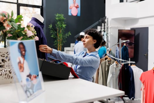 Shopping mall worker preparing store for opening, arranging fashionable merchandise on mannequin. Stylish woman waiting for customers to come and buy trendy clothes and accessories