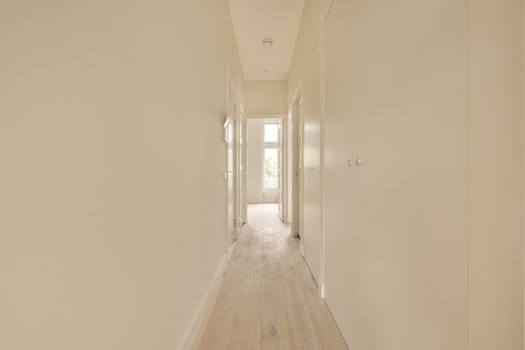 a long hallway with white walls and wood flooring on either side by side, leading to the other rooms