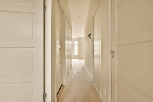 a long hallway with white walls and wood flooring on either side by side, leading to the other rooms