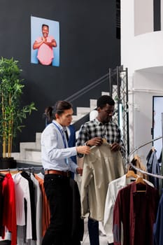 African american client checking fashionable shirt, discussing clothes material with employee in modern boutique. Shopaholic man shopping for discount outfits, buying casual wear. Fashion concept