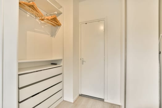 a walk - in closet with white walls and wooden flooring on the left handrails, there is an open door leading