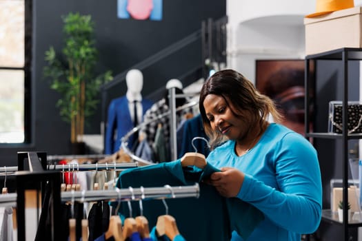 African american woman checking shirt fabric in modern boutique, shopping for fashionable merchandise. Shopaholic customer buying formal wear clothes in clothing store. Fashion concept