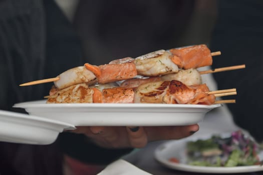 A waiter serves barbecued scallops in a plastic plate at a fair