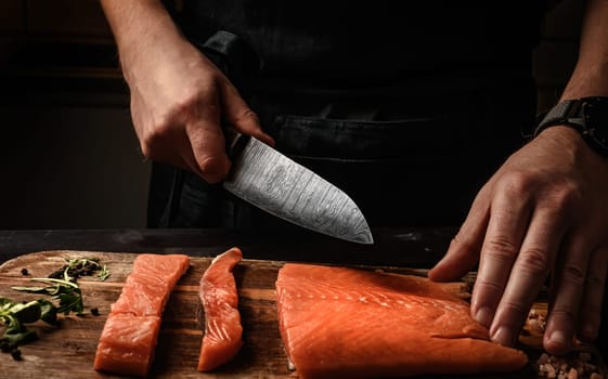 Mle cutting red Salmon fish on a cutting board with a big kitchen knife