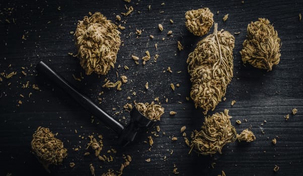 Dried CBD cannabis buds and a metal smoking pipe on a dark wooden background