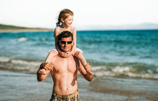 Father holding daughter at shoulders at sea coast portraits. Family dad and little pretty child kid at beach at summer together