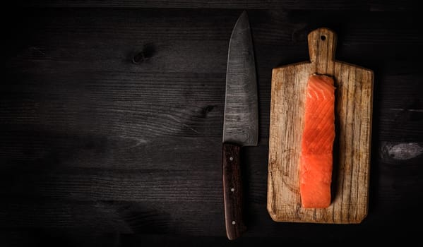 fillet of raw salmon red fish on a cutting board with a big kitchen knife, top view with a copy space