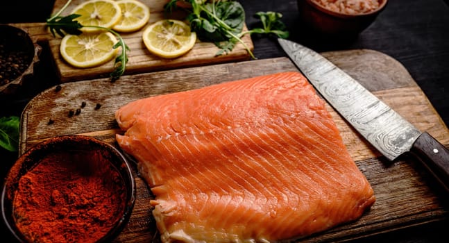 Raw salmon fillet with knife, spicies and lemons on wooden table. Healthy red omega fish and green basil at kitchen