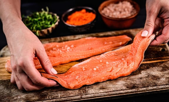 Woman cooking fillet trout with herbs and salt for dinner. Fresh red fish healthy food.