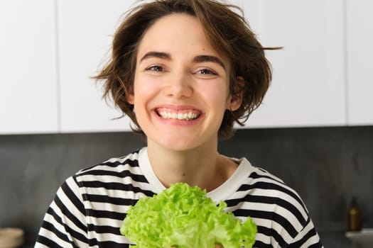 Close up portrait of beautiful, healthy smiling woman, posing with green lettuce leaf, cooking diet meal, preparing vegetarian salad, looking happy.