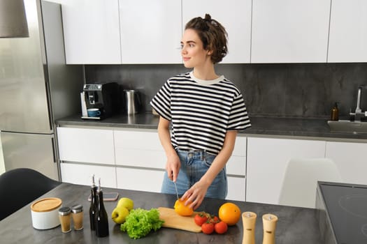 Portrait of young female model cooking in the kitchen, chopping vegetables, vegan girl preparing meal, healthy diet concept.