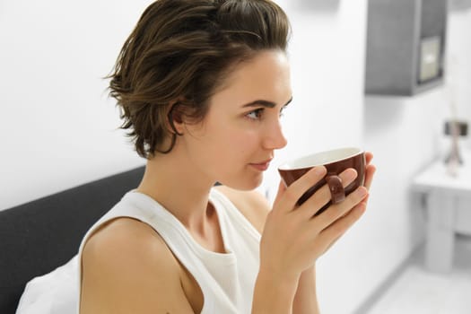 Portrait of woman smelling coffee, drinking morning cup in bed, waking up. Lifestyle concept