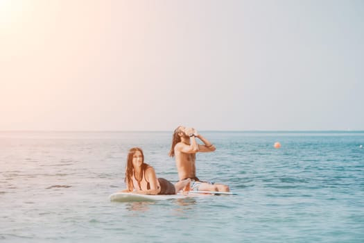 Sea woman and man on sup. Silhouette of happy young woman and man, surfing on SUP board, confident paddling through water surface. Idyllic sunset. Active lifestyle at sea or river