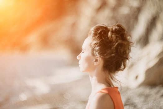 The woman in a red suit practicing yoga on stone at sunrise near the sea. Young beautiful girl in a red bathing suit sits on the seashore in lotus position. Yoga. Healthy lifestyle. Meditation