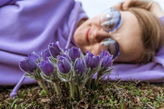 Dream grass woman spring flower. Woman lies on the ground and hugs flowers pasqueflower or Pulsatilla Grandis flowers.