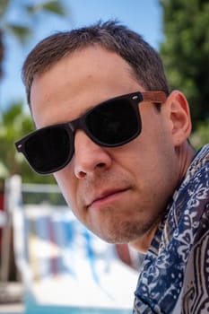 Close-up portrait of a man in black glasses at sea. Handsome man on vacation looking at camera.