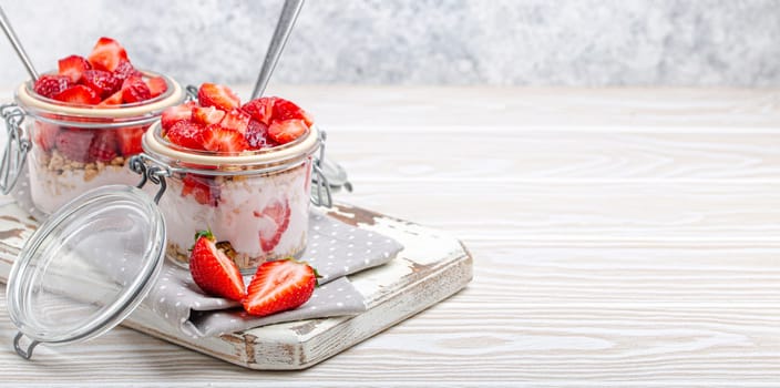 Parfait with Fresh Strawberries, Yoghurt and Crunchy Granola in Transparent Glass Mason Jars on White Rustic Wooden Background Angle View, Healthy Breakfast or Light Summer Dessert, Copy Space