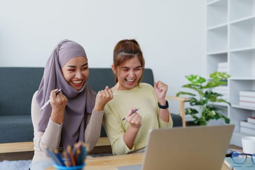 Muslim undergraduate students and Asian women express their joy after completing online study using a computer