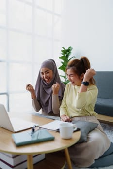 Muslim undergraduate students and Asian women express their joy after completing online study using a computer