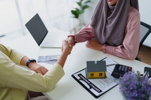 A female Muslim bank employee, holding hands, negotiates a residential loan with a customer