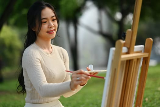 Smiling young woman painting a picture in the park. Mindfulness, art therapy and creative hobbies concept.