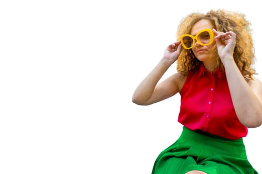 Young blonde woman with long curly hair in red and green fashion closes in sun glasses playful smile happy positive adjusts his glasses