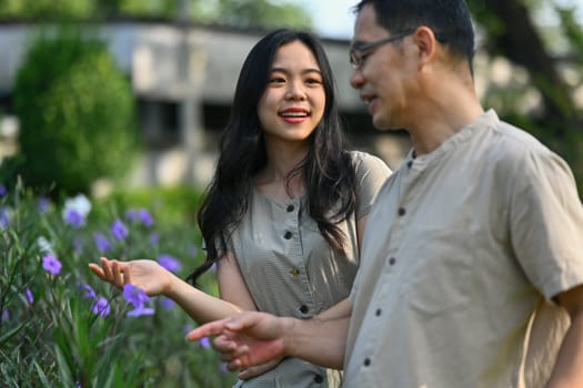 Shot of pretty young woman and middle age father admiring view of plants and flowers in public park.