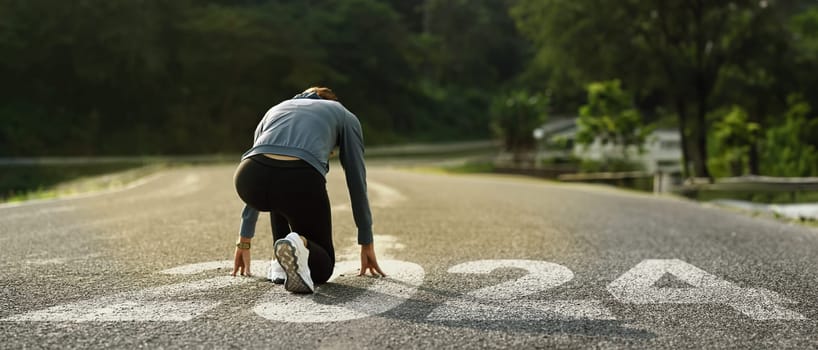 Back view of female runner in starting position on road with numbers 2024 getting ready for the new year.