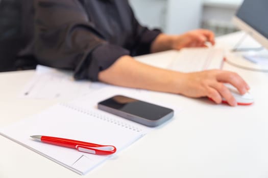 A notebook with a pen and an office worker or student in the background working on a computer