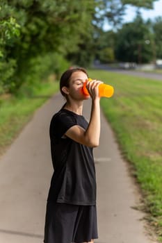 Fit tennage girl runner outdoors holding water bottle. Fitness woman taking a break after running workout.