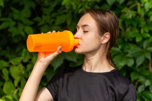 Fit tennage girl runner outdoors holding water bottle. Fitness woman taking a break after running workout.