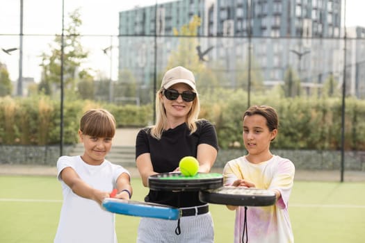 Young tennis trainer in activewear holding racket held by one of two cute girls while consulting her during individual training on stadium. High quality photo