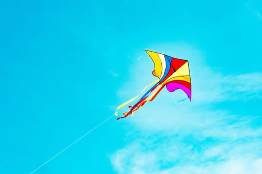 Rainbow kite flying in blue sky in sunny day in summer. Childhood concept.