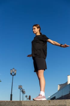 Young, fit and sporty girl in black clothes stretching after the workout in the urban city park. Fitness, sport, urban jogging and healthy lifestyle concept.