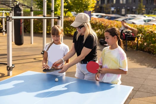 Young woman with her daughters playing ping pong in park. High quality photo