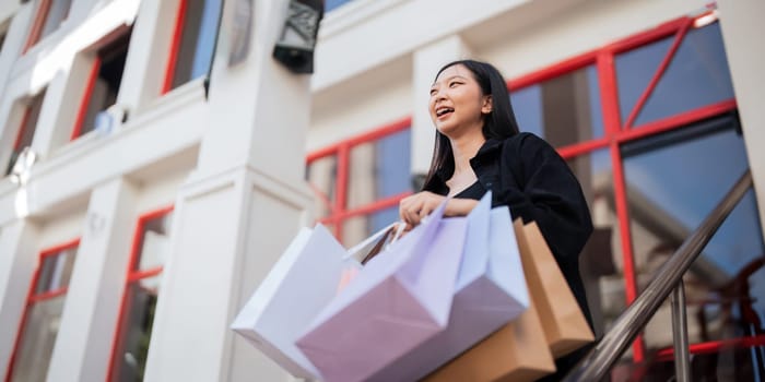 Happy beautiful young stylish woman with shopping bag while walking come out of mall on holiday Black Friday.