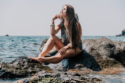 Woman travel sea. Young Happy woman in a long red dress posing on a beach near the sea on background of volcanic rocks, like in Iceland, sharing travel adventure journey