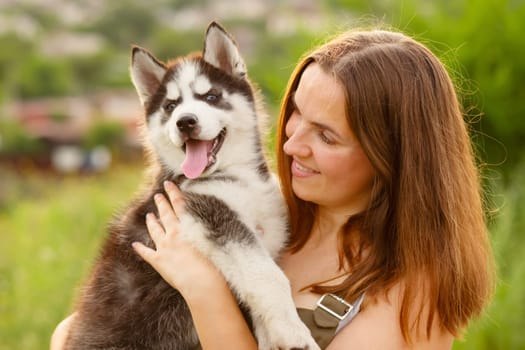 Woman playing with cute little husky puppy dog outdoors. Pet and owner love.