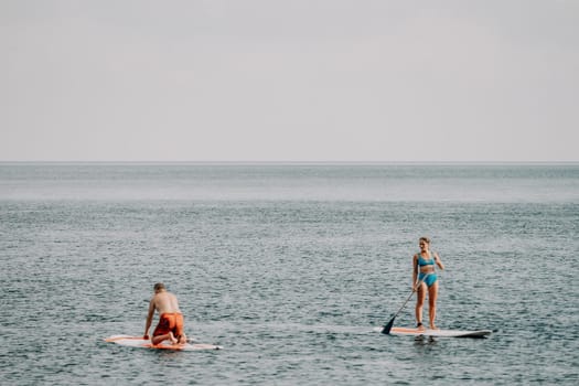 Active mature male paddler with his paddleboard and paddle on a sea at summer. Happy senior man stands with a SUP board. Stand up paddle boarding - outdor active recreation in nature