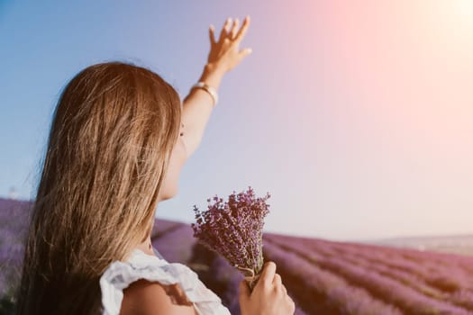 Close up portrait of young beautiful woman in a white dress and a hat is walking in the lavender field and smelling lavender bouquet.