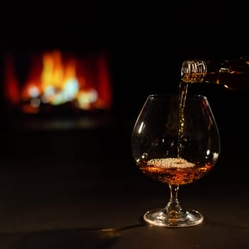 Pour brandy into a glass against the background of the fireplace.