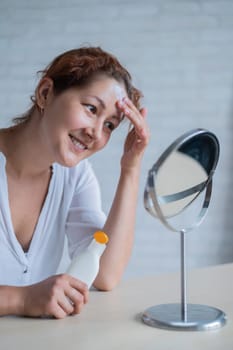 Portrait of a Caucasian woman with vitiligo uses sunscreen. A girl with a white pigment spot on her forehead looks in the mirror and is smeared with cream