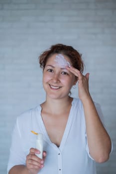 Vitiligo. Portrait of a woman with lack of skin pigmentation on her forehead. Girl smears sunscreen on a white spot on the skin of the face. Autoimmune disease