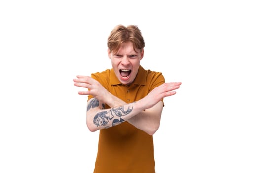 young red-haired caucasian male student with a tattoo dressed in an orange t-shirt feels angry and screams.