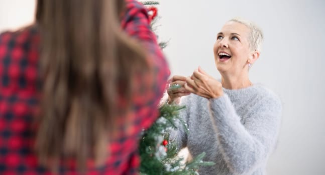 Happy senior woman with adult daughter decorate christmas tree at home.