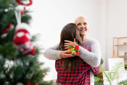Young woman giving present to happy mother and embrace indoors at home at Christmas.