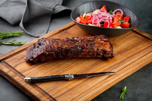 well-done steak with tomato and cucumber salad on a wooden tray
