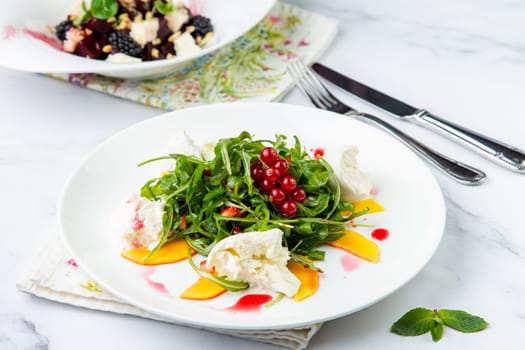 arugula salad with peach slices and red berries on a white plate