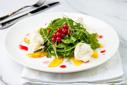 arugula salad with peach slices and red berries on a white plate