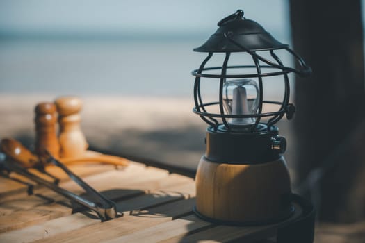 Camping by the beach with antique charm, A kerosene lamp and a modern LED lantern on a wooden table. Nature's beauty and modern equipment make for a unique experience.
